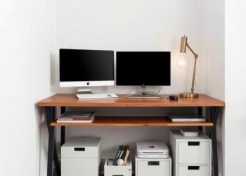 A small home office with a wooden desk, two monitors, and organized under-desk storage boxes.