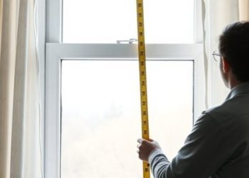 A person measuring a window with a tape measure for curtain fitting.