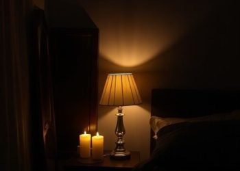 A moody bedroom with a lamp and candles providing soft lighting.