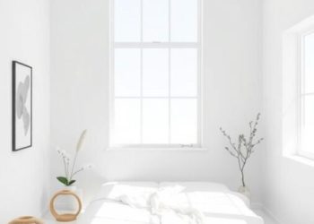 A bright, minimalist white bedroom with a bed, large windows, and simple decor.