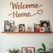 A warm family photo display with a 'Welcome Home' sign, framed pictures, and decorative plants.