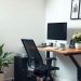 A modern ergonomic home office desk setup with a black chair, computer monitor, and a plant.