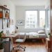 A cozy multi-functional home office with a desk, chair, bed, and plants.