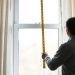A person measuring a window with a tape measure for curtain fitting.