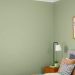 A bedroom featuring a sage green accent wall, light bedding, and a ceiling fan.