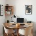 A small home office with a round table, two chairs, a wall-mounted shelf, and a warm color scheme.