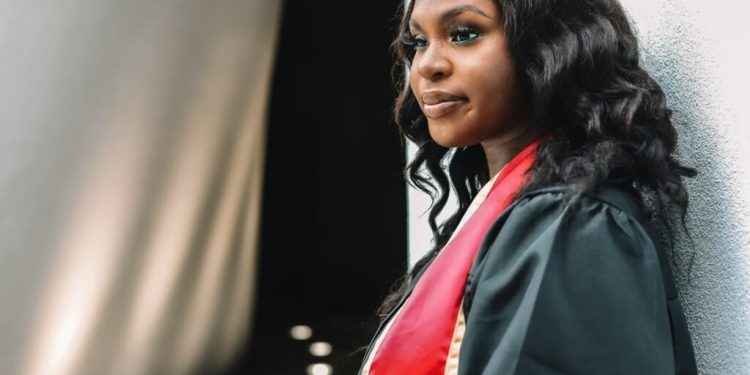 a woman in a graduation gown leaning against a wall