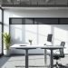 A modern adjustable desk in a bright office space with a plant and computer.