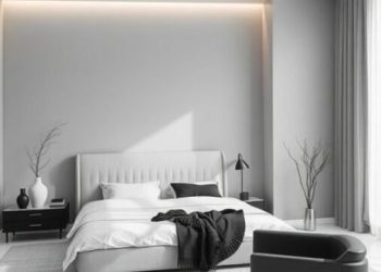 A minimalist bedroom featuring a gray color scheme, a bed with white linens, a black accent chair, and natural decor elements.