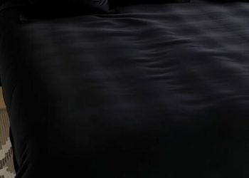 Luxurious black velvet bed with golden-accented pillows and a stylish bedside lamp.