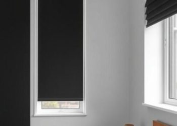 A minimalist bedroom featuring black blackout shades over two windows, with a white bedding set on a bed.