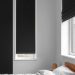 A minimalist bedroom featuring black blackout shades over two windows, with a white bedding set on a bed.