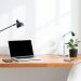 A minimalist desk setup featuring a laptop, smartphone, and a small potted plant on a wooden desk.