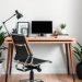 A minimalist desk setup featuring a wooden desk, a computer monitor, a desk lamp, and plants.
