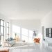 A minimalist living room featuring an open space concept with large windows, light furniture, and simple decor.