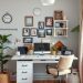 A bright home office with a desk, computer, framed photos on the wall, and plants.