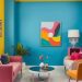 A vibrant living room featuring a blue accent wall, pink and yellow furniture, and colorful artwork.