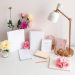 A feminine home office desk arrangement with notebooks, flowers, and a lamp.