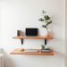 A minimalist floating desk setup with two wooden shelves, a laptop, books, and a plant.