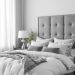 A grey bedroom featuring a plush bed with grey bedding, a tufted headboard, and light curtains.