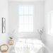A bright, minimalist white bedroom with a bed, large windows, and simple decor.