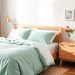 A cozy bedroom featuring mint green bedding, wooden furniture, and a natural rug.