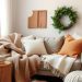A cozy living room with a sofa covered in warm textiles, including blankets and pillows in earthy tones, alongside a knitted pouf and a woven basket.