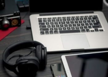 A modern work from home setup featuring a laptop, tablet, smartphone, and headphones on a desk.