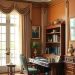 A traditional home office featuring a wooden desk, green chair, bookshelves, and warm-toned walls.