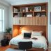 A home office featuring a Murphy bed, a desk with a laptop, and shelves with books and plants.