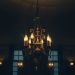 A vintage chandelier with candle-like bulbs, casting a warm glow in a dimly lit room.