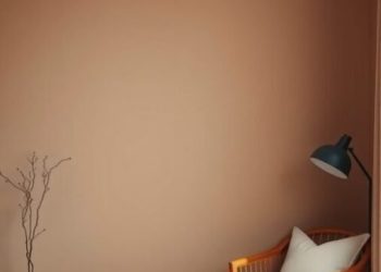 Minimalist bedroom corner with warm taupe walls, a wooden chair, and a side table.